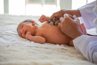 doctor hands use stethoscope to check health of newborn baby and take care him or treat the disease or disorder. baby is not wearing any clothes and look like feel cold and lie on white mat on bed.