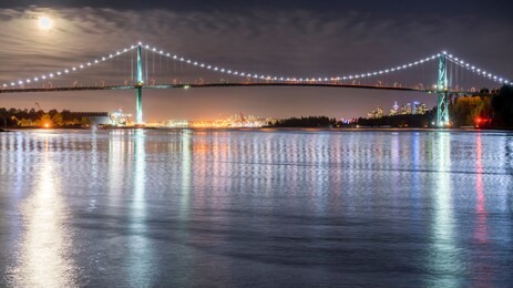 vancouver, british columbia. canada view at night of the lions gate bridge with lights trail, glitters and clouds on a full moon sky.