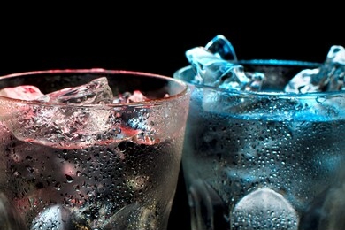 two colorful, cold cocktails with transparent ice on a black background. cocktails of red and blue in glass with ice cubes. party in the club entertainment. mixed light.
