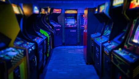 old vintage arcade video games in an empty dark gaming room with blue light with glowing displays and beautiful retro design on a wide landscape photo