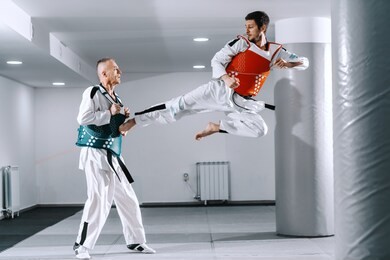 two caucasian sporty men sparring in tekwondo fittings in gym with bucklers on.