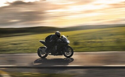 man riding a sports motorbike at sunset, flying by with a field in the background.