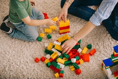 cropped view of mom and son playing with toy blocks on carpet