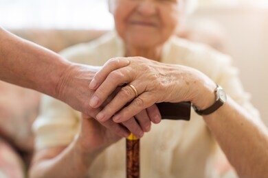 close-up of woman holding senior's hands leaning on walking cane