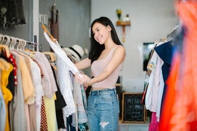 positive woman choosing new clothes in shop and smiling