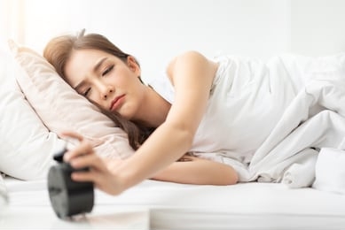 sleepy asian woman turning off alarm clock while sleepy. girl is having trouble waking up late in morning.