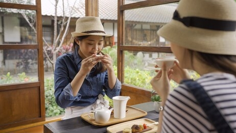 cheerful girlfriends spending time together at japanese local cafe kyoto talking and laughing happily. young girls travelers holding tea bowl drink. friendship teenager communication diversity relax
