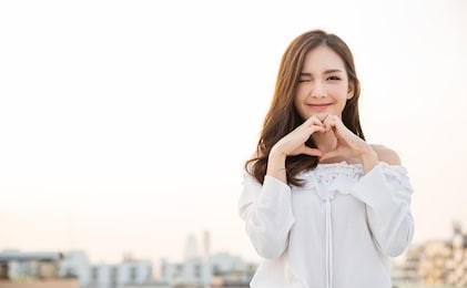 portrait of young beautiful asian woman hands gesture in heart shape on city sky roof top. smile face asian girl wear casual cloth. japanese girl lifestyle, love valentines’ day concept 