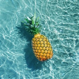 ripe pineapple into water on sunny beach. top view.
