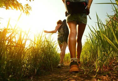 two young ladies walking with backpacks through green lush meadow