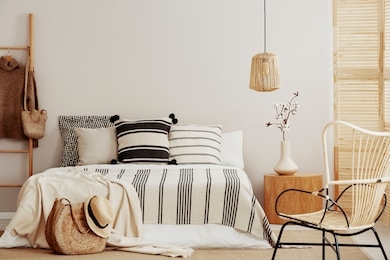 striped bedding on comfortable king size bed in contemporary bedroom interior with wicker chair and copy space on empty wall