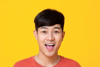 studio portrait of  handsome young asian man face smiling with mouth open isolated on colorful yellow background