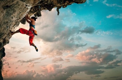 athletic woman climbing on overhanging cliff rock with sunrise sky background