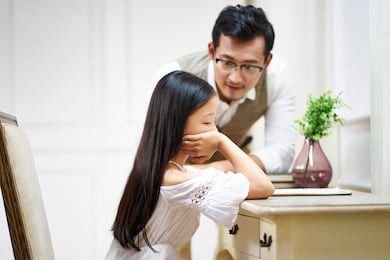 sad little asian girl sitting at desk in her room and getting comfort from caring father
