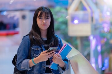 portrait of young asian female student using her mobile phone sending a text outside at university