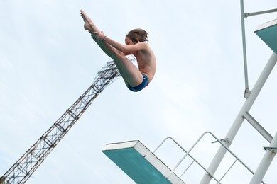 a young athlete performs 1/2 somersault platform 5m in the center of the city in an outdoor pool against the backdrop of an urban view