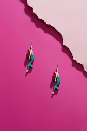 shot of massive earrings with pendants in the view of storybook mermaid. the accessory set is isolated asymmetrically on pink background, near pale pink ragged platform. stylish women's fashion item.