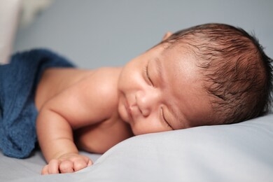 portrait close up studio shot two month old smiling newborn baby is sleeping 
on his stomach on gray blanket