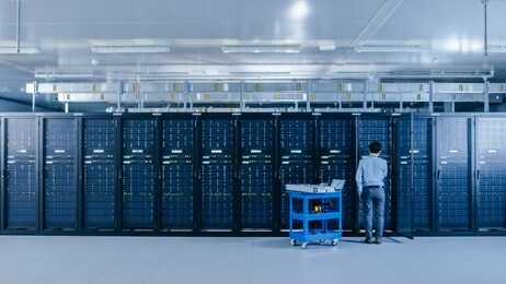 in the data center: it engineer working with server racks works with opened cabinet to installs new hardware for system update, cart stands beside the row of server racks. engineer doing maintenance.