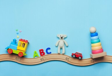 toys background with copy space. kids toys train, abc letters, bear, car and pyramid on toy wooden railway on blue background with blank space for text. top view, flat lay.