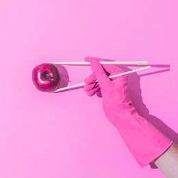 hand in pink glove holds chopsticks with apple. creative concept of healthy eating and japanese traditional food. 