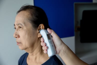 doctor checking patient's temperature in the ear with tympanic thermometer, inside the hospital or clinic. temperature elderly person .