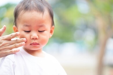 mother applying face skin with sun screen cream on her baby boy in playground park.