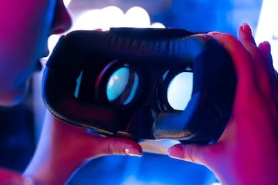 female hands holding 3d 360 vr headset glasses in futuristic purple blue neon light, woman experience wearable virtual augmented ar reality digital innovation technology concept, close up view