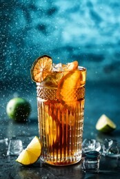 fresh cocktail with cola, lime, orange and ice in glass on dark blue background. studio shot of drink in freeze motion, drops in liquid splash. summer cold drink and cocktail