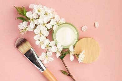 cosmetic jar with skin care cream top view pink pastel colored background with make up brush and fresh white flower blossom twig. 
