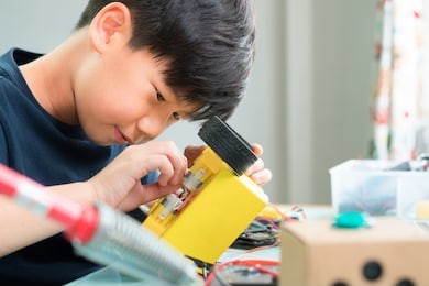 closeup: smart looking asian boy working with circuits, wires, computer chip, oled, motor, wheels on his robotics project. science, technology, engineering and mathematics (stem) education concept.