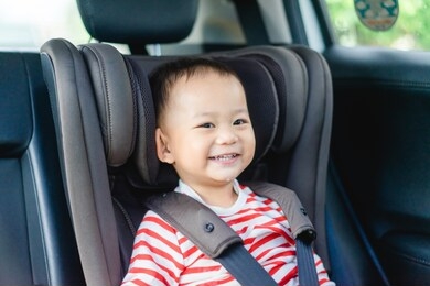 transport, safety, childhood road trip and people concept - happy little asian boy showing front teeth with big smile,laughing and face covered in milk drop.baby boy sitting in baby car seat.