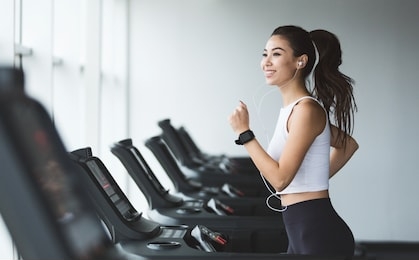 young woman exercising on treadmill and listening music in the gym, copy space