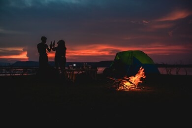 silhouette  group of asian friends tourist drinking and playing guitar together with happiness in summer while having camping near lake 
