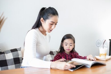 mom is teaching her daughter to read a book.
