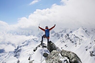 mountaineer with ice ax stands on the top of a mountain in the background of the landscape of snowy mountains