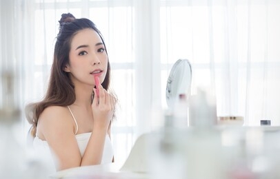 closeup portrait of young beautiful asian girl put lipstick on with mirror for makeup routine. beauty woman with perfect glow skin dress up. health care lifestyle cosmetic blogger influencer concept