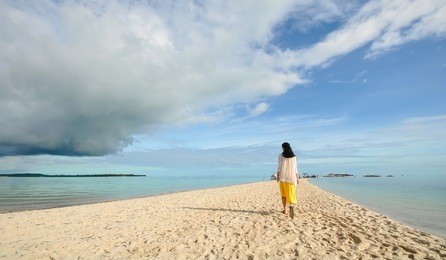 back portrait of single young girl walking on long curving stretch of narrow white sand beach during low tides. shot on virgin island, panglao, bohol, philippines.