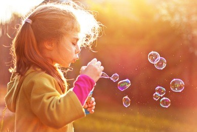 five years old caucasian child girl blowing soap bubbles outdoor at sunset - happy carefree childhood