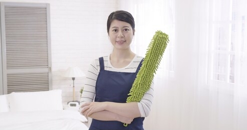 happy smiling confident professional asian woman domestic worker holding green feather duster. girl housework homework helper. proud chinese wife in apron face camera arms crossed attractive smile.