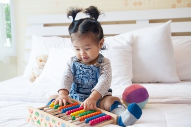 cute little baby girl playing with abacus at home in sunny kids room