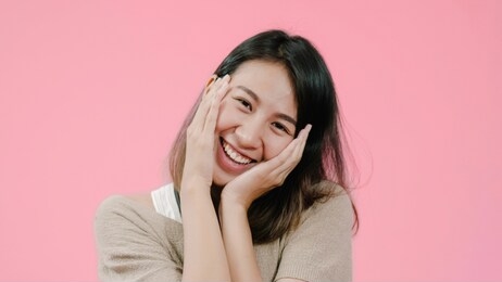 smiling adorable asian female with positive expression, smiles broadly, dressed in casual clothing and looking at the camera over pink background. happy adorable glad woman rejoices success.