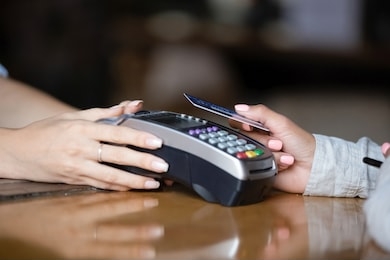 close up woman, customer paying by plastic contactless credit card with  waitress holding card reader machine in hands on wooden bar counter, contactless payment concept