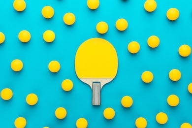 racket and many balls for table tennis on turquoise blue background. flat lay image of many table tennis balls with tennis paddle in the middle. minimalist photo of yellow ping-pong equipment
