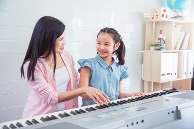 beautiful asian pianist teacher teaching a girl to play piano, music education concept.