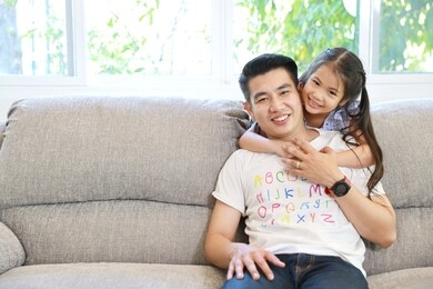 happy asian family daughter hugging father on grey sofa in living room with happy smiling face (lifestyle concept)