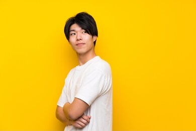 asian man over isolated yellow wall with arms crossed and happy