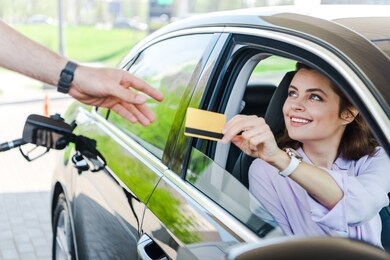 selective focus of happy woman sitting in car and giving credit card to worker at gas station 