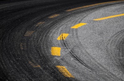 abstract turning road background with tires track and yellow striped road marking on dark asphalt