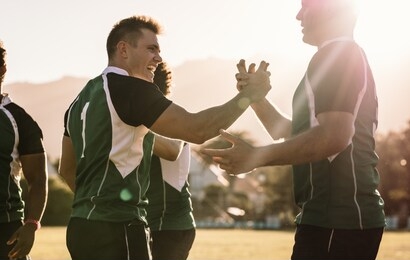 rugby winning team players shaking hands and smiling after winning the game. sportsmen in uniform celebrating the victory on field outdoors.
